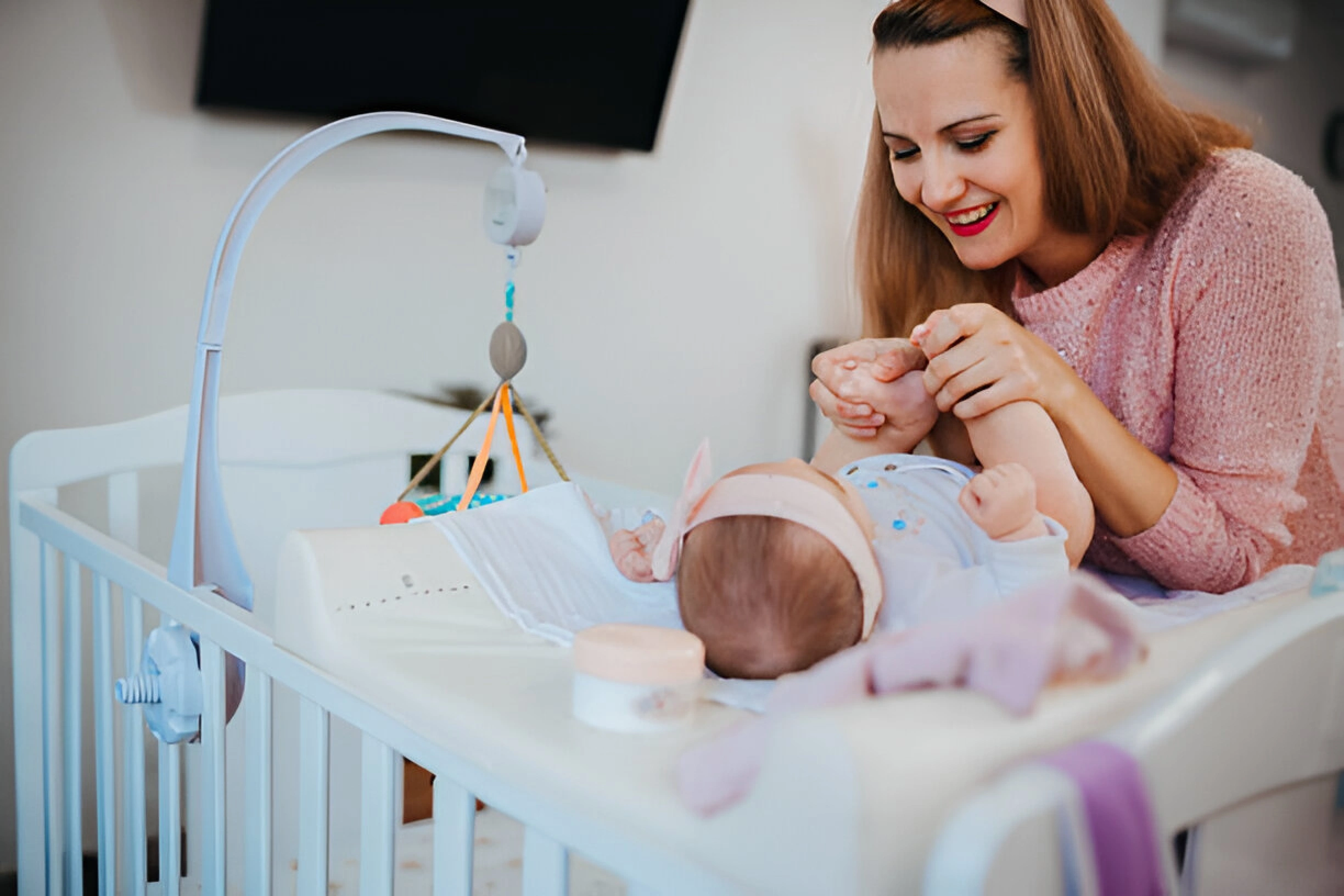 A mother is spending time with her child safely lying in the crib.